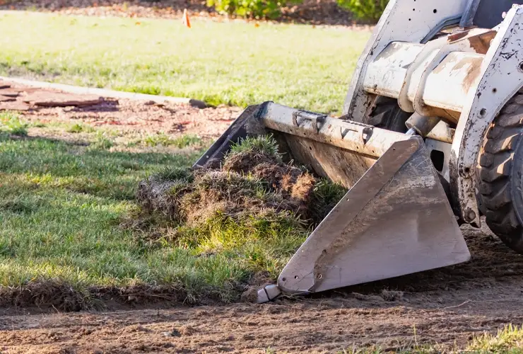 A large construction excavator with a raised bucket digging into the ground, preparing a landscaping site in Florida