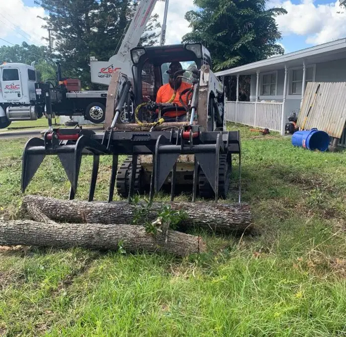 HomeGrownOutdoors worker using a grapple machine to clear heavy logs, providing professional tree care services in Florida.
